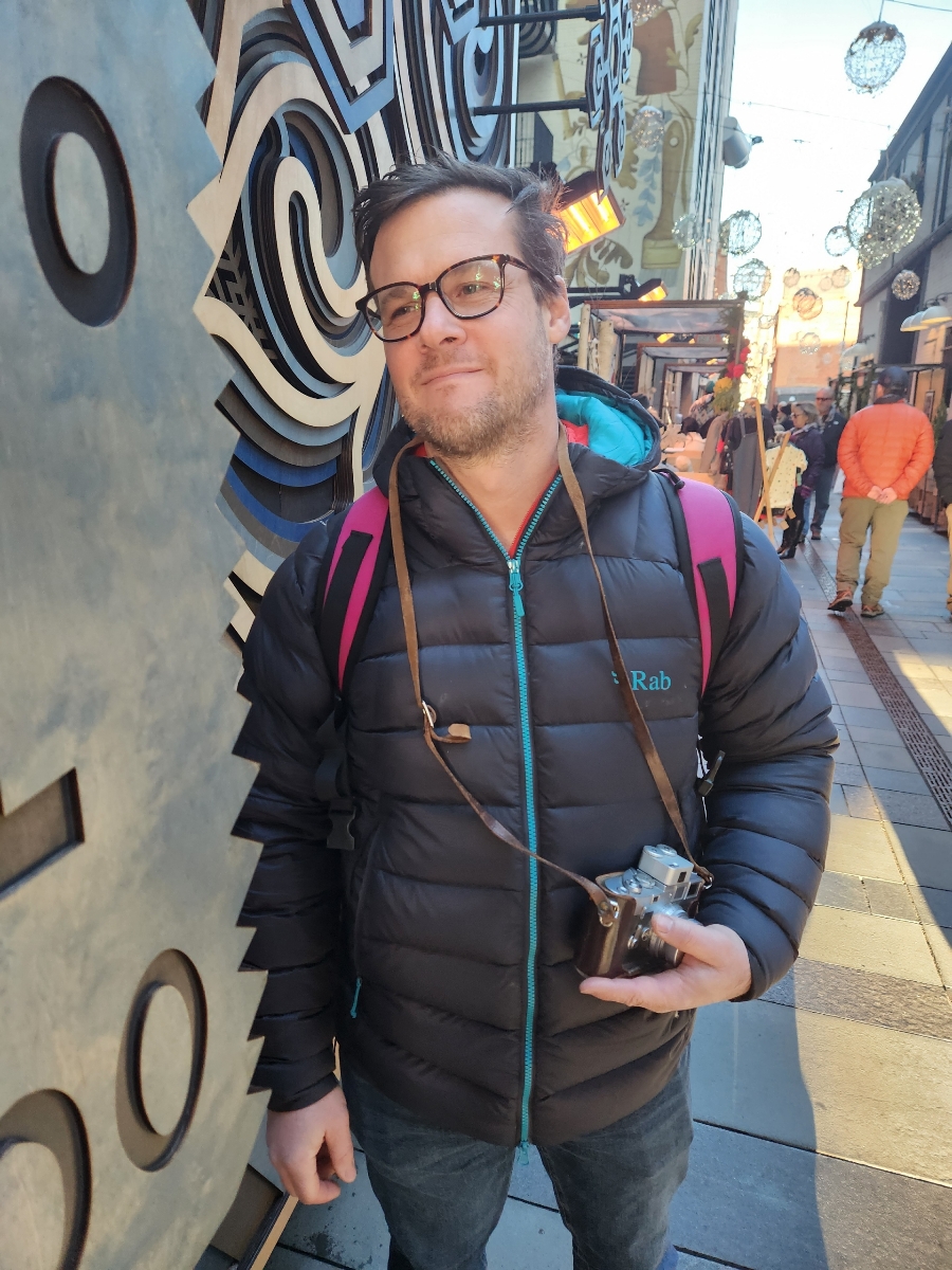 A photo of Matty, the owner, on an urban street, holding a Leica M3 camera.
